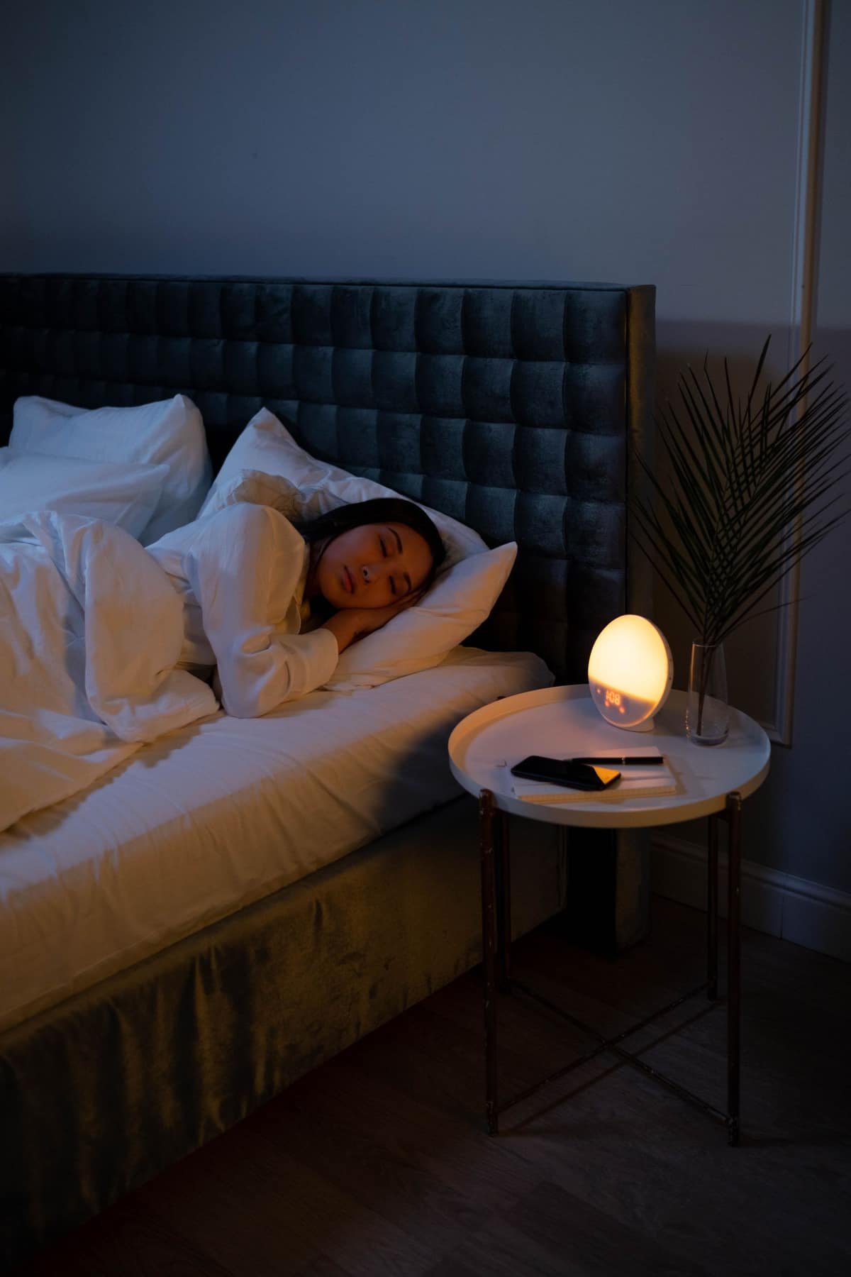 Woman sleeping in a dark bedroom with a warm bedside lamp