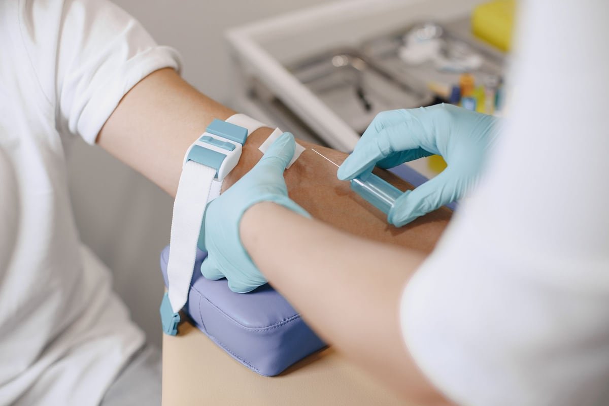 Healthcare professional wearing blue gloves drawing a blood sample from a patient&rsquo;s arm in a clinic to check vitamin levels