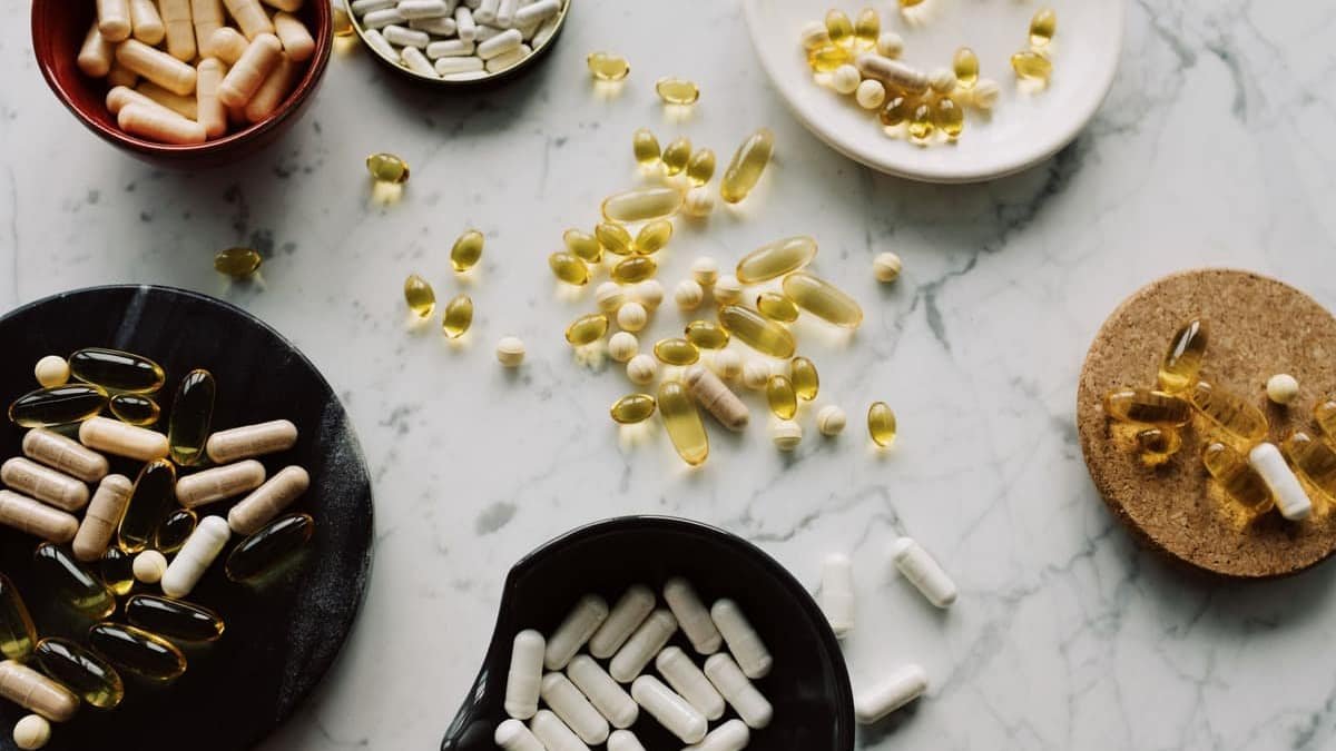 Assorted supplement capsules and softgels spread across a marble surface