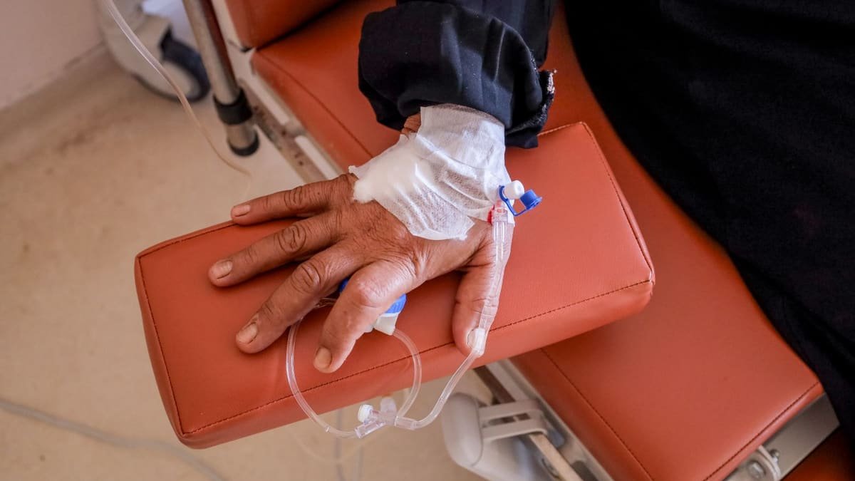 A patient's hand resting on an infusion chair armrest with an IV line taped in place
