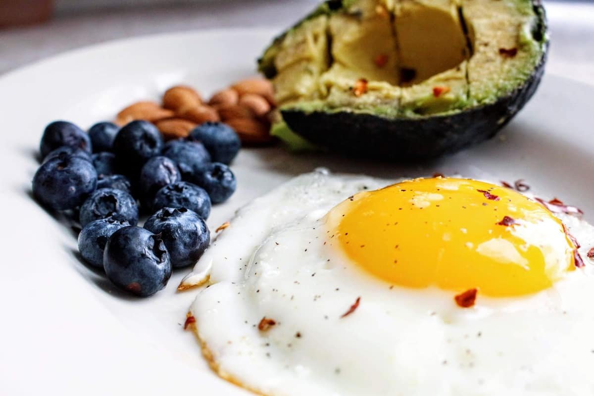 White plate with a fried egg, blueberries, almonds and half an avocado