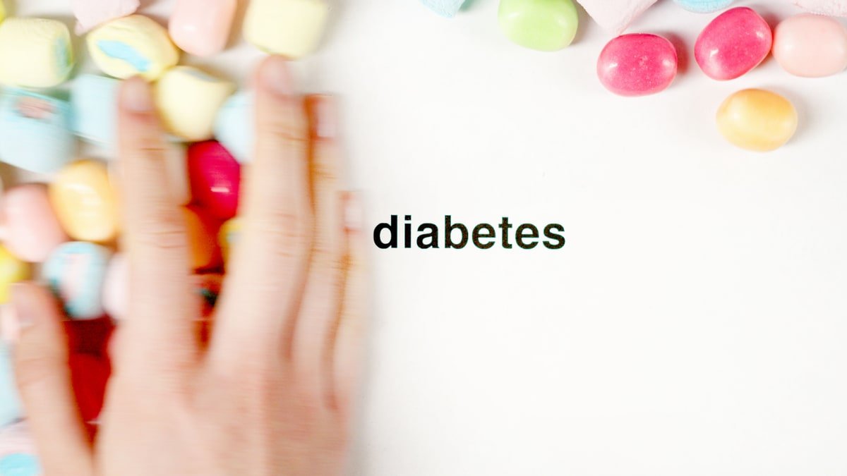 A hand gently pushes pastel candies away from the word &lsquo;diabetes&rsquo; on a white background &mdash; a visual metaphor for reducing sugary foods to support nerve health