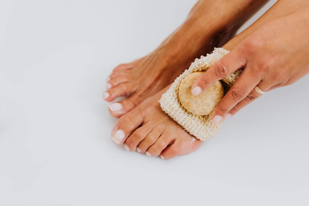 Hands gently washing a bare foot with soap in a sisal pouch