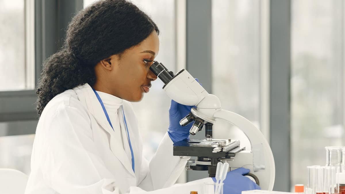 Scientist in a lab coat looking through a microscope in a bright laboratory